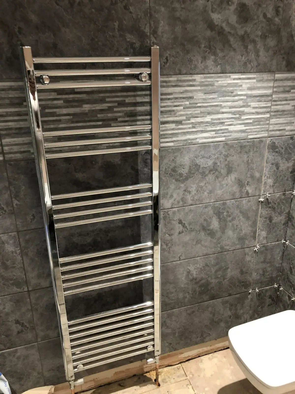 Chrome heated towel rail on grey tiles