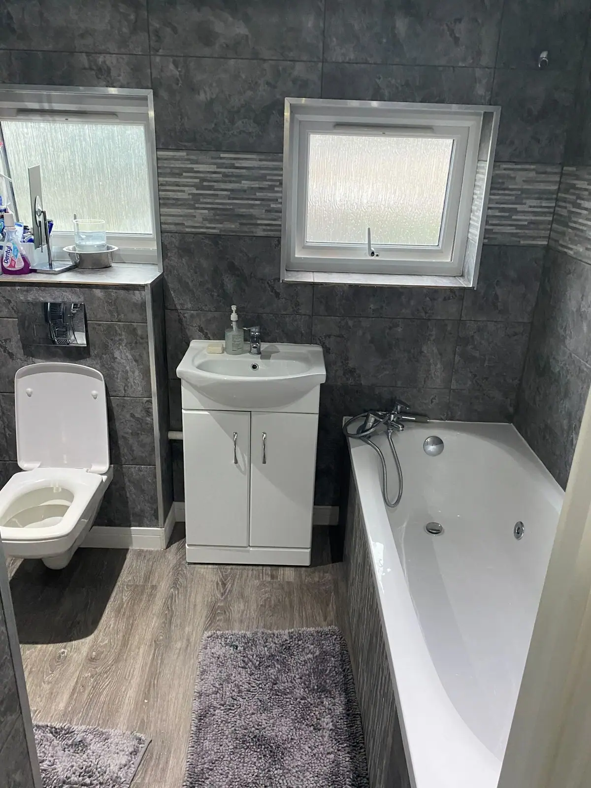 Refitted bathroom with grey tiles, whirlpool bath and vanity unit